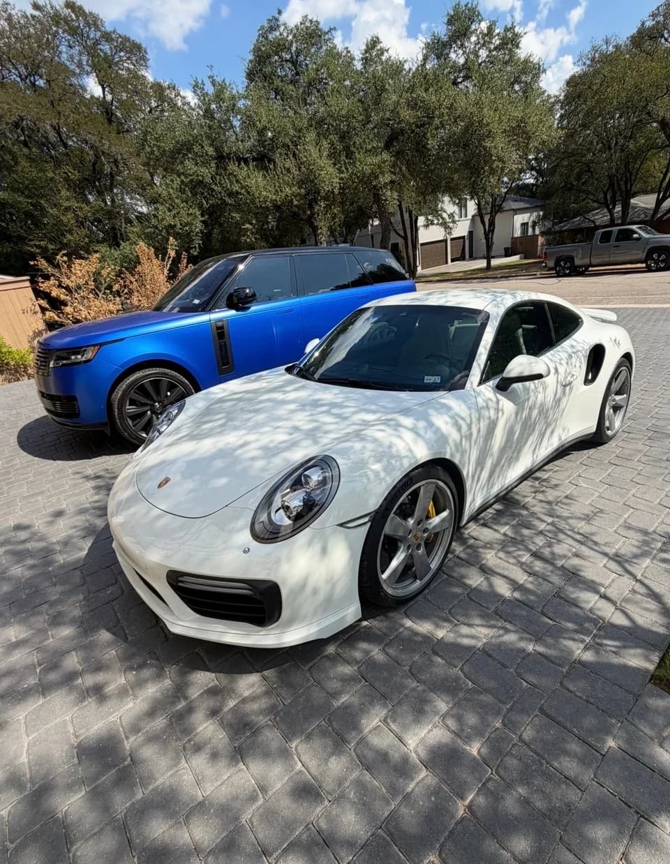 White Porsche parked beside a blue Range Rover